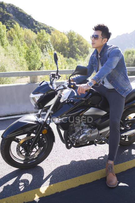 Chinese man sitting on motorcycle on highway — Stock Photo
