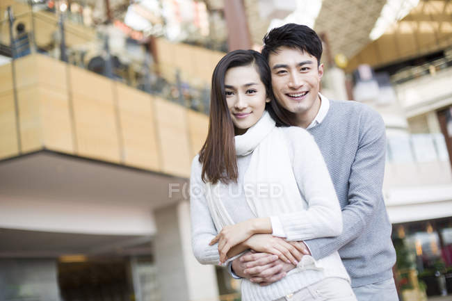 Young Chinese couple embracing in shopping mall — Stock Photo
