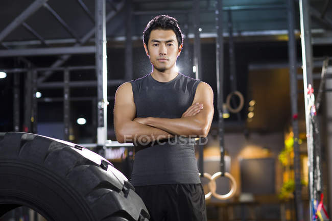 Chinese man standing at gym with arms folded — Stock Photo