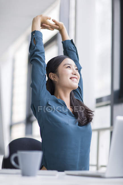 Chinese businesswoman stretching in office — Stock Photo