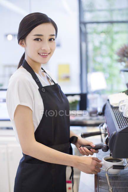 Chinese barista standing at coffee maker and looking in camera — Stock Photo