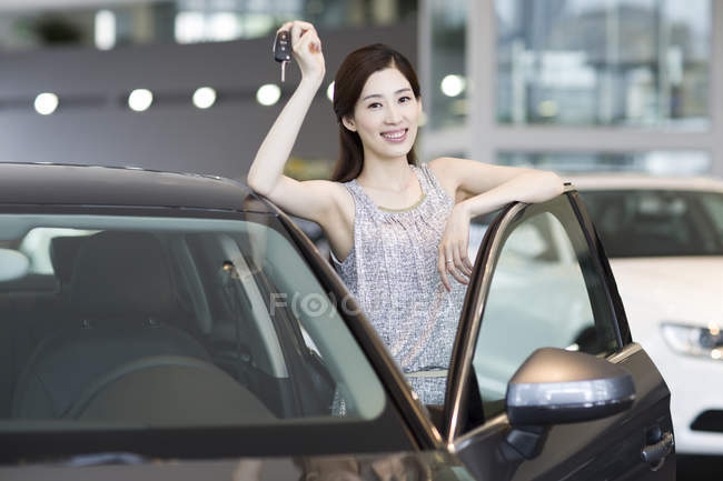Chinese woman holding keys to new car in showroom — Stock Photo