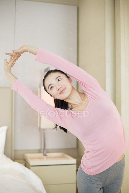 Chinês mulher em rosa sportswear alongamento no quarto — Fotografia de Stock