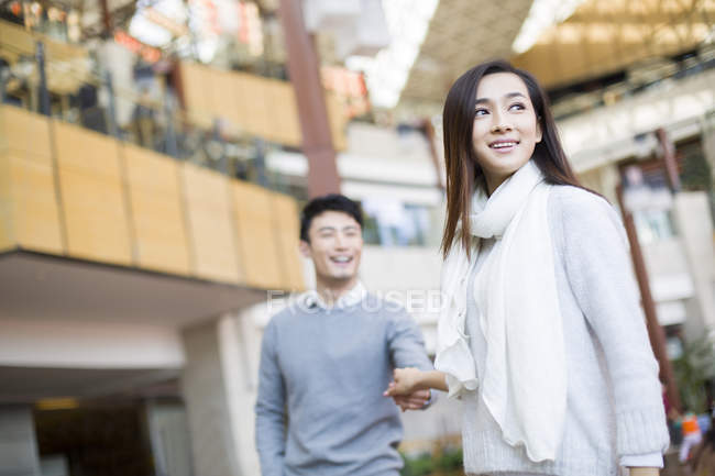 Mujer china y hombre tomados de la mano mientras compran en el centro comercial - foto de stock