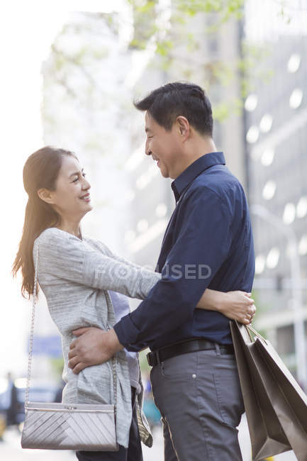 Reifes chinesisches Paar umarmt sich mit Einkaufstüten in der Stadt — Stockfoto