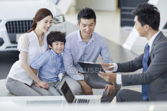 Distribuidor de coches chinos sentado con la familia de los clientes en sala de exposición - foto de stock