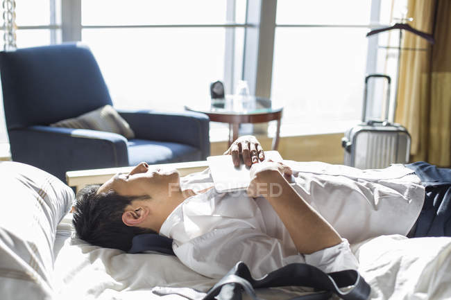 Chinese businessman resting on bed in hotel room — Stock Photo