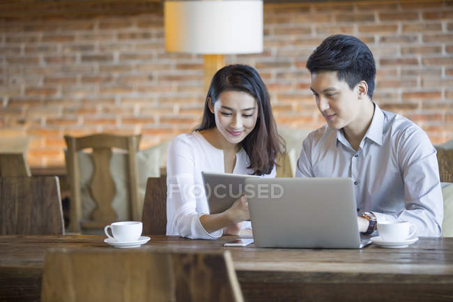 Uomo e donna cinese che utilizzano tablet e laptop digitali nel caffè — Foto stock