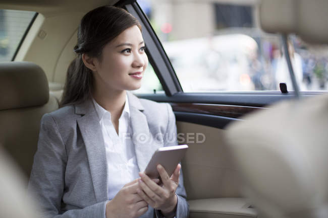 Chinese woman holding smartphone in car — Stock Photo