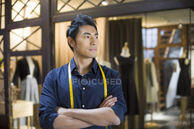 Chinese male fashion designer standing in shop with arms folded — Stock Photo