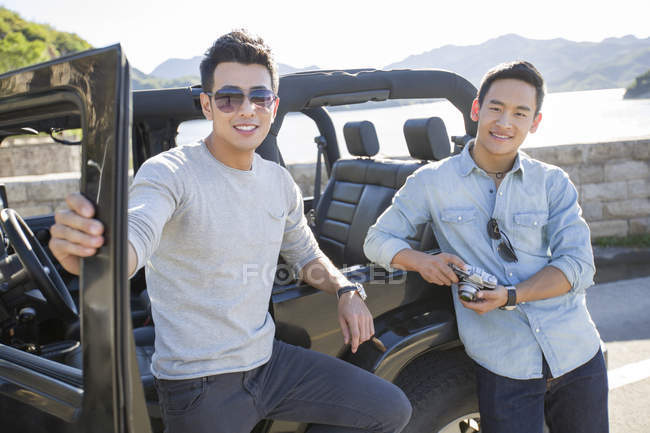 Chinese men leaning on car in suburbs and looking in camera — Stock Photo