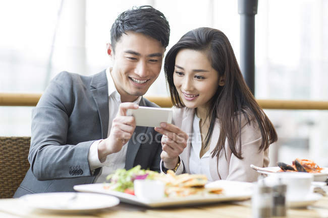 Pareja china tomando fotos con smartphone en el restaurante - foto de stock