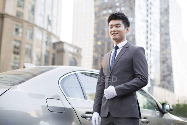 Chófer chino de pie delante del coche - foto de stock