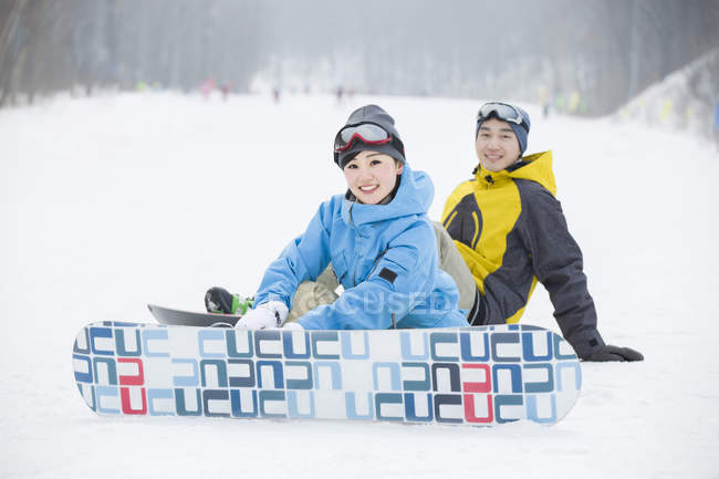 Couple chinois assis avec snowboards sur neige — Photo de stock
