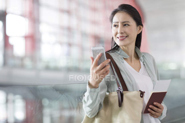 Mulher chinesa segurando smartphone e bilhete no aeroporto — Fotografia de Stock