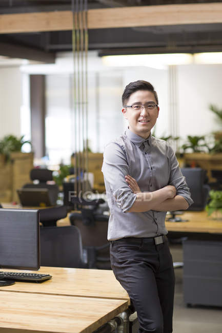 Trabajador de oficina chino de pie en la oficina con los brazos cruzados - foto de stock