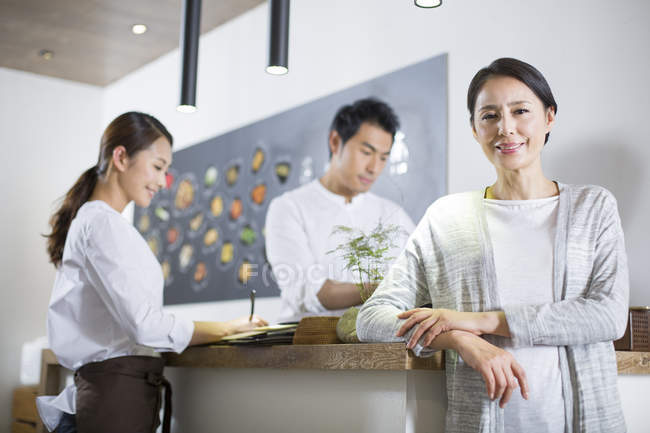 Propietario de restaurante chino apoyado en el mostrador con personal de espera - foto de stock