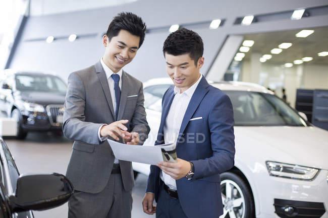 Chinese businessman making deal with car seller in showroom — Stock Photo
