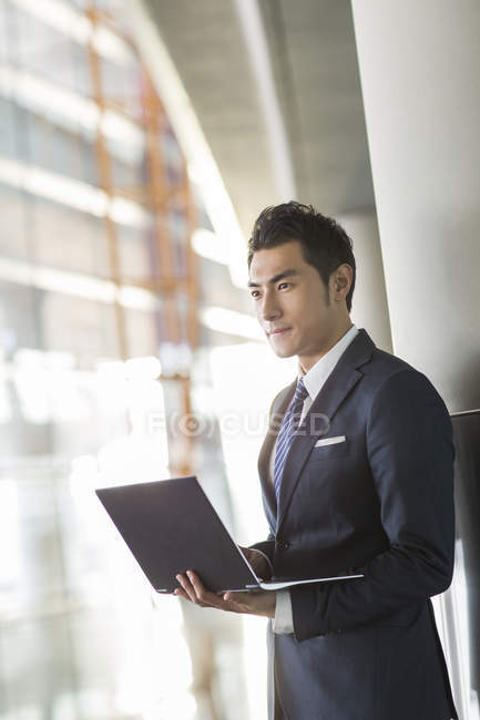 Homme d'affaires chinois debout avec ordinateur portable à l'intérieur — Photo de stock