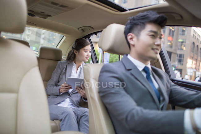 Chófer chino conduciendo coche con la mujer de negocios en el asiento trasero - foto de stock