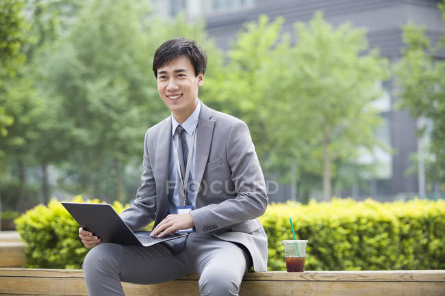 Chinesischer Geschäftsmann sitzt mit Laptop auf Straße — Stockfoto