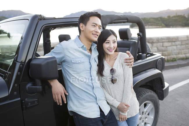 Chinese man hugging woman in front of car — Stock Photo