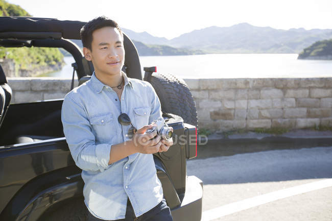 Китаец стоит с цифровой камерой на берегу озера — стоковое фото