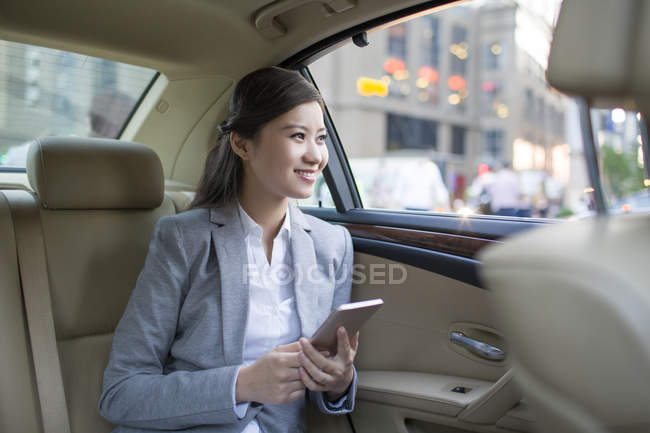 Chinese woman holding smartphone on car back seat — Stock Photo