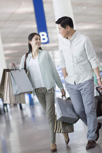Casal chinês maduro andando no aeroporto com sacos de compras — Fotografia de Stock