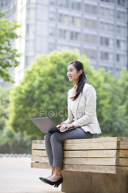 Empresária chinesa sentada com laptop no banco — Fotografia de Stock