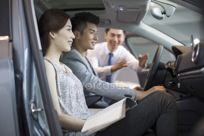 Chinese car dealer helping couple choosing car in showroom — Stock Photo