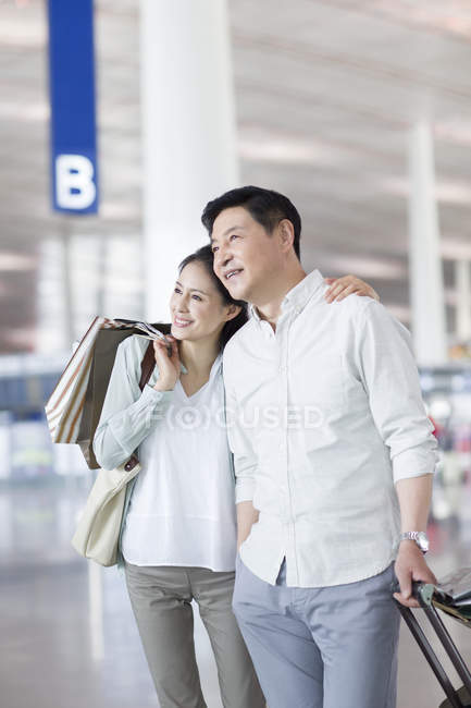 Mature chinese couple standing at airport with shopping bags — Stock Photo
