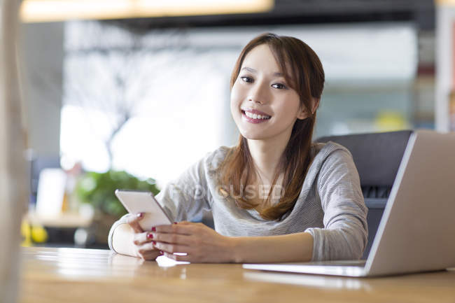 Chinese woman holding smartphone at office desk — Stock Photo