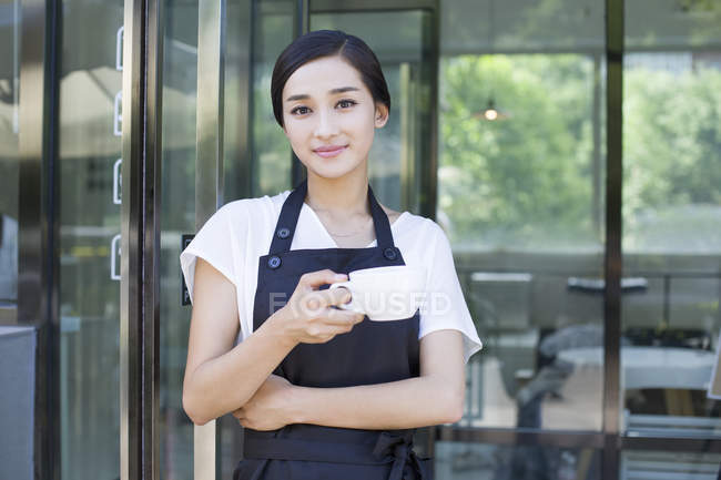 Ladenbesitzer steht mit Tasse Kaffee vor Tür des Cafés — Stockfoto