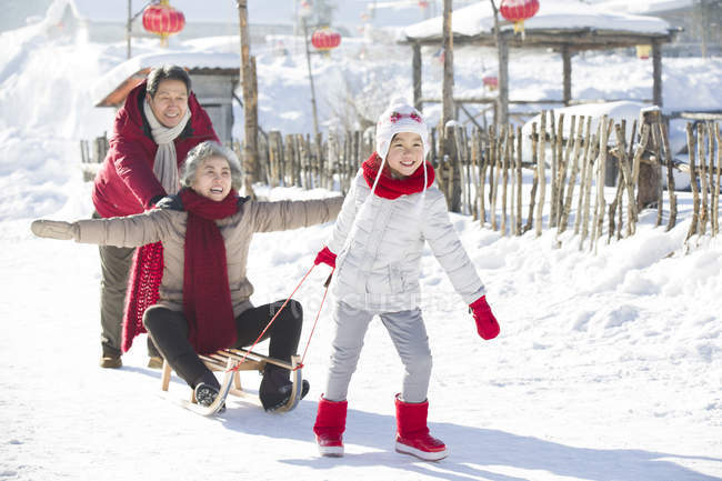 Chinese girls pulling sled with grandparents in snow — Stock Photo