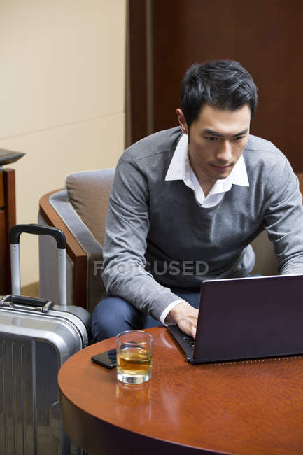 Homme d'affaires chinois utilisant un ordinateur portable à la table dans la chambre d'hôtel — Photo de stock