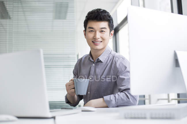 Chinese businessman drinking coffee at workplace — Stock Photo