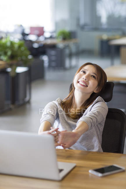 Chinese woman stretching hands at workplace — Stock Photo