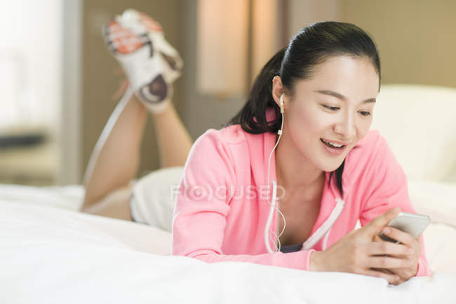 Mulher chinesa ouvindo música com smartphone na cama — Fotografia de Stock