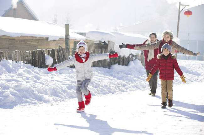 Avós chineses correndo na neve com crianças — Fotografia de Stock