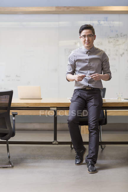 Chinese man leaning on desk in board room — Stock Photo