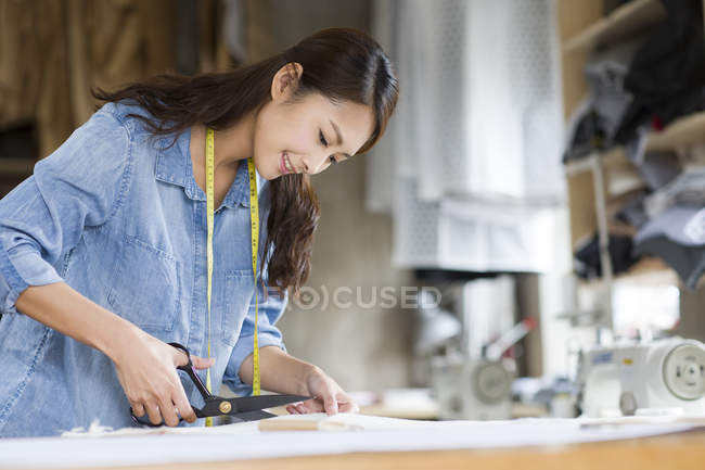 Chinese fashion designer working in studio with scissors — Stock Photo