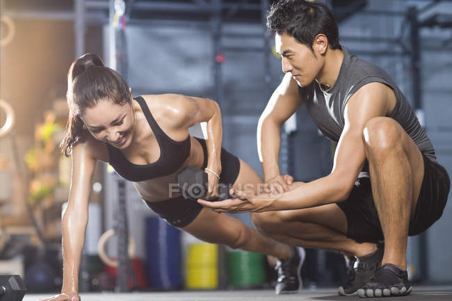 Chinese woman doing push-ups with trainer in gym — Stock Photo