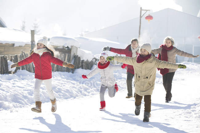 Chinese grandparents running in snow with children — Stock Photo