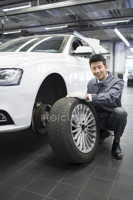 Meccanico cinese auto tenendo ruota auto in officina — Foto stock