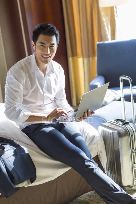 Empresário chinês usando laptop na cama no quarto de hotel — Fotografia de Stock