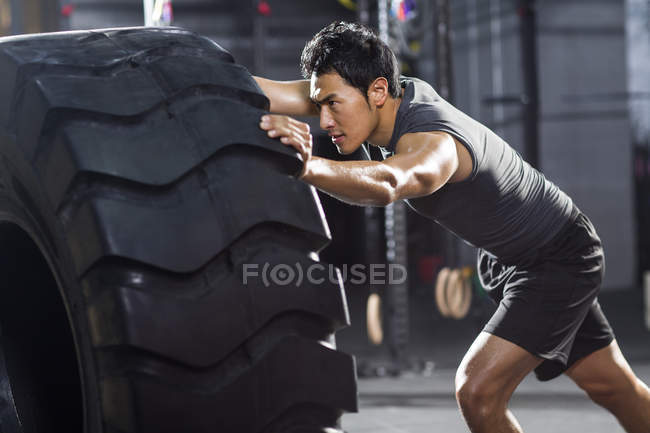 Chino hombre empujando grande neumático en crossfit gimnasio - foto de stock