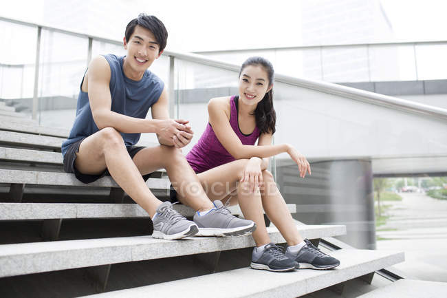 Chinese couple resting on stairs after exercising — Stock Photo