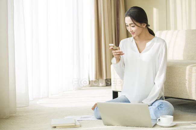 Китайська жінка, що вдома за допомогою смартфона і ноутбук — стокове фото