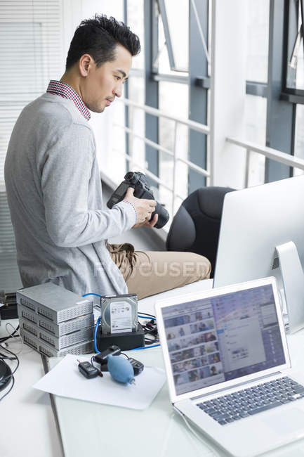 Chinese photographer sitting on desk in office — Stock Photo